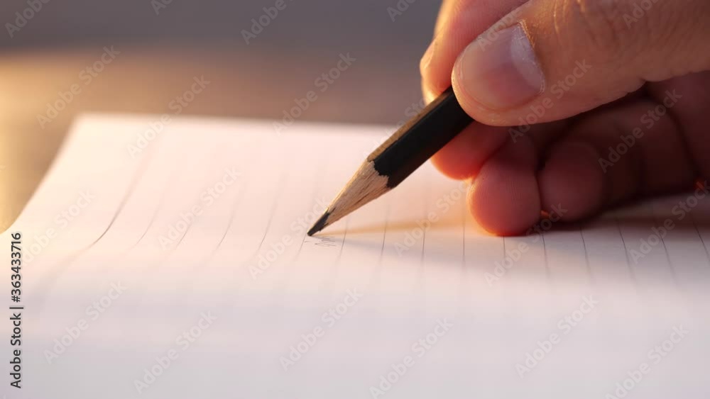 Close up of hand holding pencil and writing on paper Close up of hand holding pencil and writing on paper