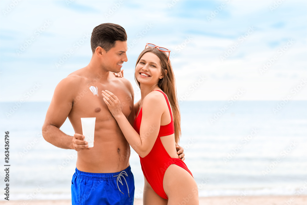 Young couple applying sunscreen cream on sea beach Young couple applying sunscreen cream on sea beach