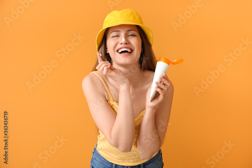 Foto Young woman applying sunscreen cream against color background