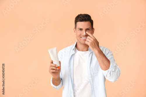 Young man applying sunscreen cream against color background