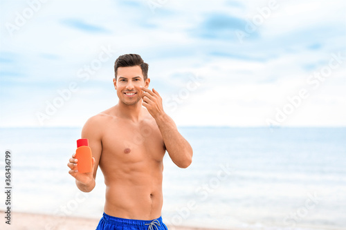 Young man applying sunscreen cream on sea beach