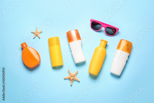 Bottles of sunscreen with sunglasses on color background