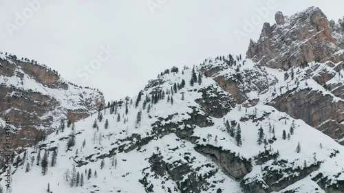 Aerial view of the high mountains in the Fannes-Sennes natural park in Alto Adige, Italy. Old jagged rocks covered with snow. Snowflakes flying in the air slowly. The sky is white-gray and cloudy. photo