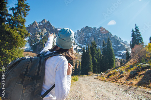 A woman with a backpack points the way. Road in mountainous terrain