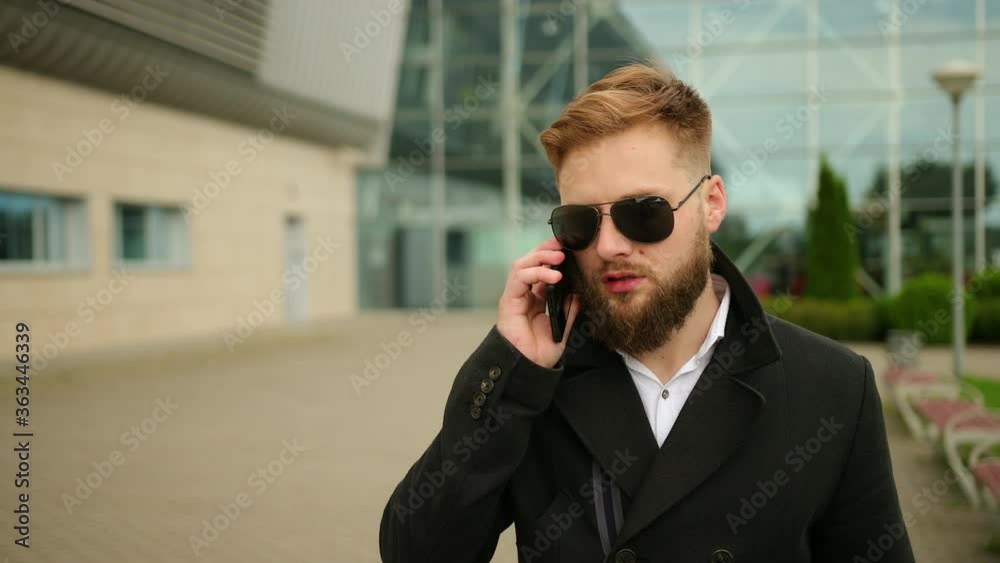 Man talking on phone outside, handsome young businessman, answering smartphone, mobile technology, telephony, business trips, wall street, sunglasses, making a call with telephone. Office buildings Man talking on phone outside, handsome young businessman, answering smartphone, mobile technology, telephony, business trips, wall street, sunglasses, making a call with telephone. Office buildings