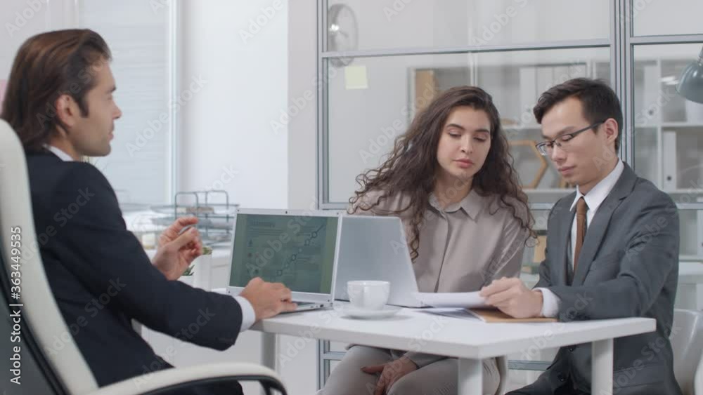 Modern business partners sitting at office desk successfully finishing collaborative bargaining with making agreement, then shaking hands