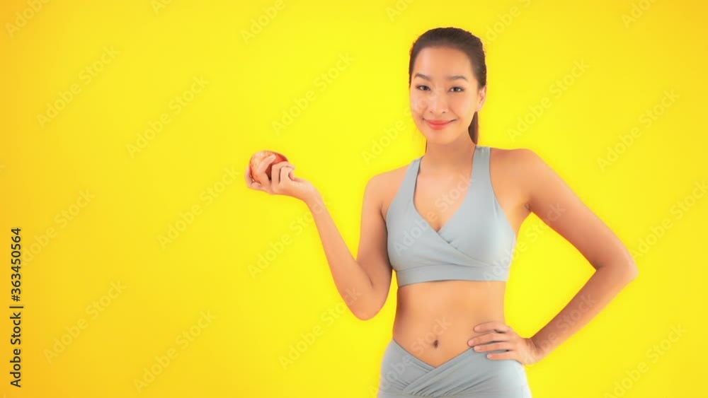 Petite Asian Fitness Female in Sportswear Showing Apple. Healthy Lifestyle Concept, Isolated on Yellow Background, Slow Motion Petite Asian Fitness Female in Sportswear Showing Apple. Healthy Lifestyle Concept, Isolated on Yellow Background, Slow Motion