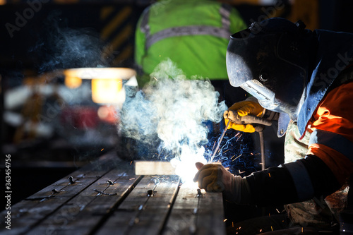 The welder is welding with covered electrode in the factory. Stick welding, is a manual arc welding process that uses a consumable electrode covered with a flux to lay the weld.
