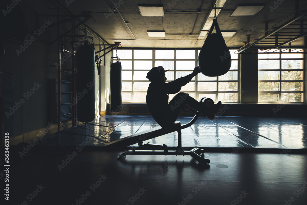 Obraz premium Trening siłowy Crossfit mężczyzny z workiem treningowym i wykonujących ćwiczenia prasowe na siłowni. Sylwetka strzału przed oknem