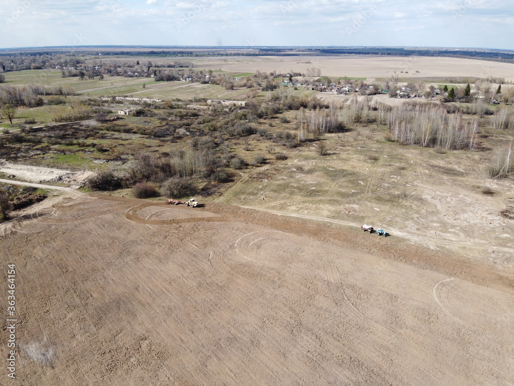 Agricultural machinery in a field near a small grove, aerial view. Agricultural land. Agricultural machinery in a field near a small grove, aerial view. Agricultural land.
