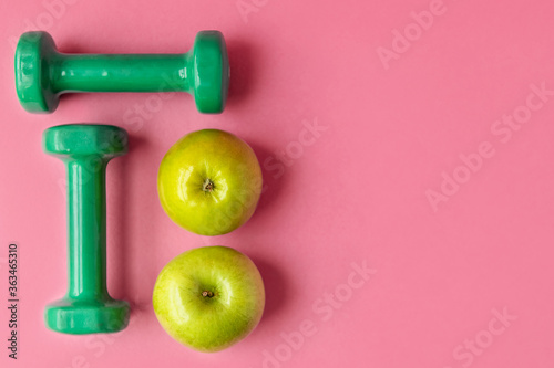 Composition with dumbbells and green apples on a pink background, top view. Concept of dietary nutrition and healthy lifestyle. copy space.