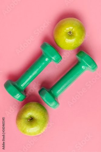 Composition with dumbbells and green apples on a pink background, top view. Concept of dietary nutrition and healthy lifestyle. copy space.
