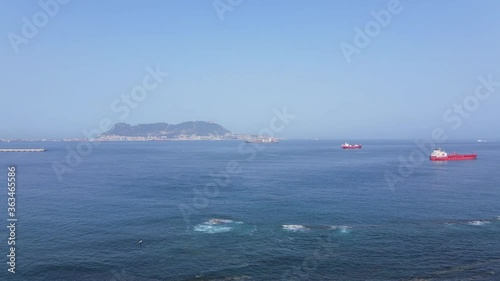 The British Rock of Gibraltar in the background on a cloudless summer day from the air. A few merchant ships can be seen in the foreground.