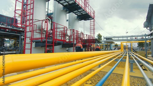 Gasman in a protective mask who walks along the gas production station and inspects it. Yellow gas distribution lines along which the gas flow is distributed.