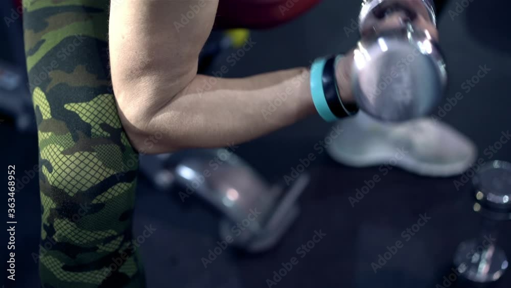 Middle-aged strong and independent woman in sportswear pumping hands muscles close-up with dumbbells in gym. Workout of athlete train inside fitness hall. Age fitness or training. Healthy lifestyle. Middle-aged strong and independent woman in sportswear pumping hands muscles close-up with dumbbells in gym. Workout of athlete train inside fitness hall. Age fitness or training. Healthy lifestyle.
