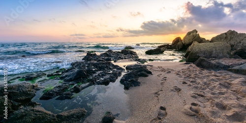 idyllic sunset on the ocean shore. waves crashing rocks on sandy beach. beautiful cloudscape above the horizon