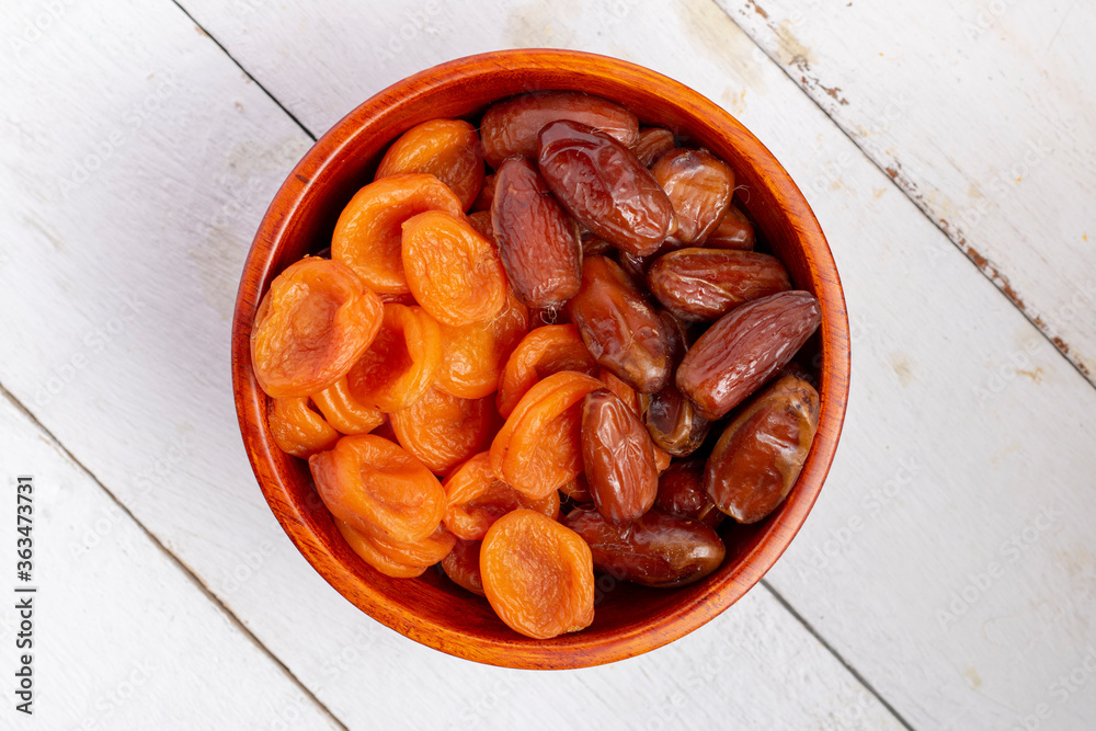 Dried apricots and dates in a wooden bowl with dates, flat lay Dried apricots and dates in a wooden bowl with dates, flat lay
