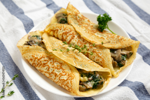 Savory Homemade Mushroom, Spinach and Cheese Crepes on a white plate on cloth, low angle view. Close-up.