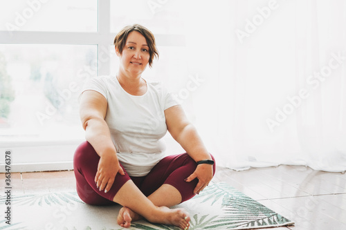Adult charming brunette woman plus size body positive practice yoga at the bright studio photo