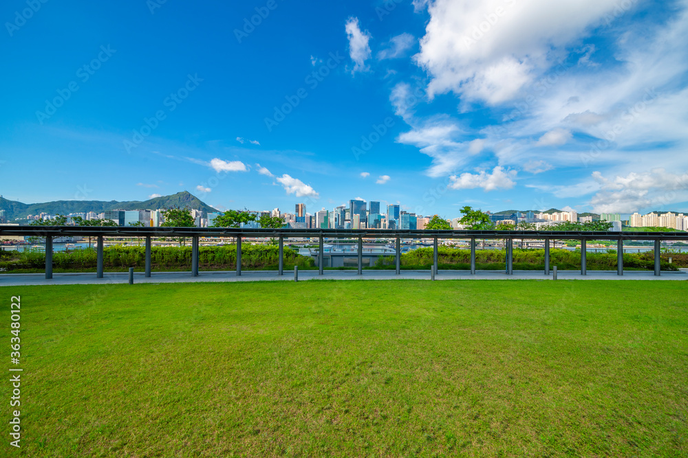 The glass walkways and lawns of the modern park in the city center are under the blue sky and white clouds.