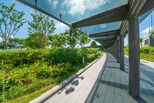 The glass walkways and lawns of the modern park in the city center are under the blue sky and white clouds.