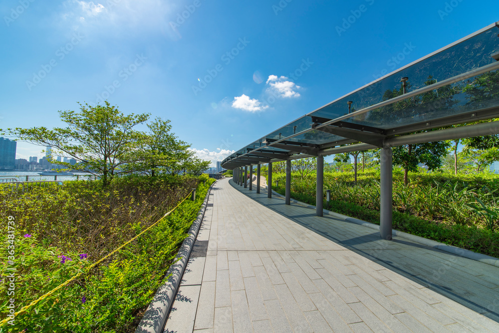 The glass walkways and lawns of the modern park in the city center are under the blue sky and white clouds.