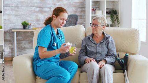 Female doctor sitting on sofa with senior woman in nursing home giving her daily pills. photo