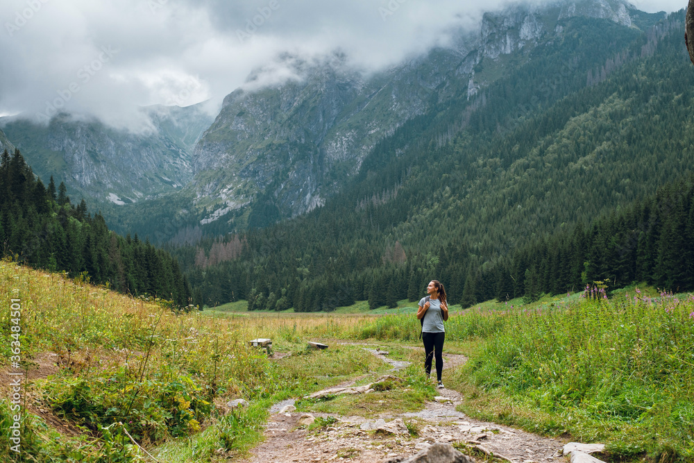Beautiful young woman with backpack hiking in beautiful Rysy mountains, Tatra, Poland, Slovakia. Green hills and rocky peaks