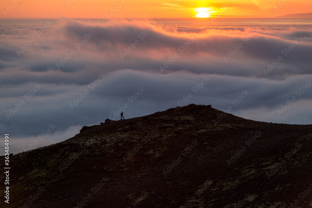 Silhouette of a man on the ridge above the sea of clouds, misty mountains at sunset in Iceland