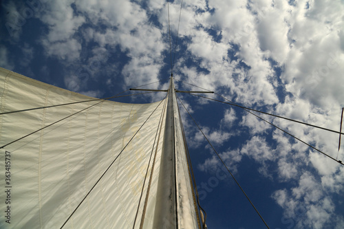 Mast of a yacht with a sail against the blue sky with white clouds. Walk on a yacht. Sailing holidays. Tourism. Travel by water. Regatta.