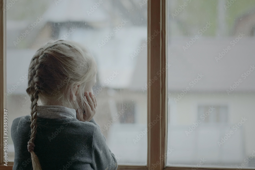 Little 5 year girl with braid hair style looking out her room foggy window, rainy weather outside Little 5 year girl with braid hair style looking out her room foggy window, rainy weather outside