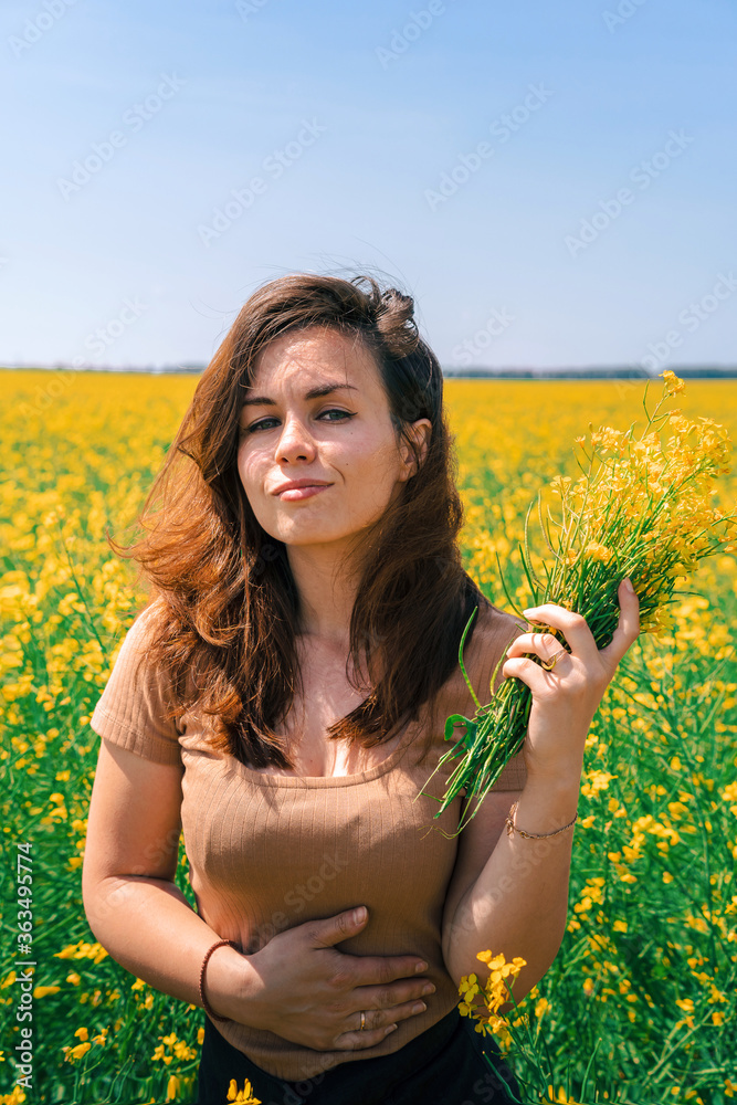 A happy young girl with long hair holds a yellow rapeseed bouquet in a thick rapeseed field, a place for text copy space A happy young girl with long hair holds a yellow rapeseed bouquet in a thick rapeseed field, a place for text copy space