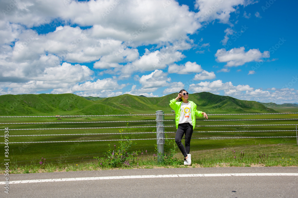 Fototapeta premium A woman in the blue sky and white clouds of the grassland road side.