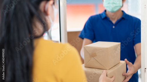 Young Asian woman wearing face mask or surgical mask signing on digital tablet for receiving package from delivery service company staff for prevent coronavirus infection during covid-19 outbreak. © pitipat