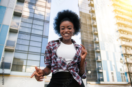 Close-up portrait young happy black African American woman with curly black hair, dressed casual. Over city background. Lifestyle.