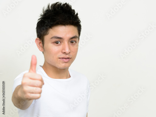 Portrait of young handsome Asian man giving thumbs up