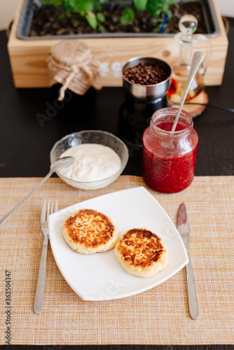 Healthy breakfast. Cheesecakes on a white plate. Breakfast in the home kitchen. Cheesecakes on a plate, next to a jar with sour cream and raspberry jam. Sour cream and raspberry jam.