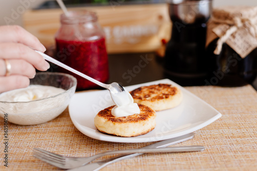Healthy breakfast. Cheesecakes on a white plate. Breakfast in the home kitchen. Cheesecakes on a plate, next to a jar with sour cream and raspberry jam. Sour cream and raspberry jam.