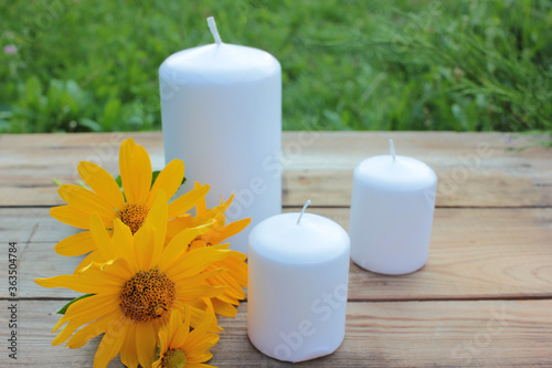 White candles and yellow flower on the wooden table in the summer garden