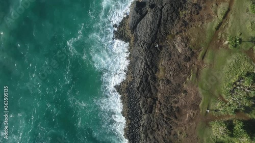 top down view of ocean white water waves against basalt cliff coastline with vegetation and walking paths.