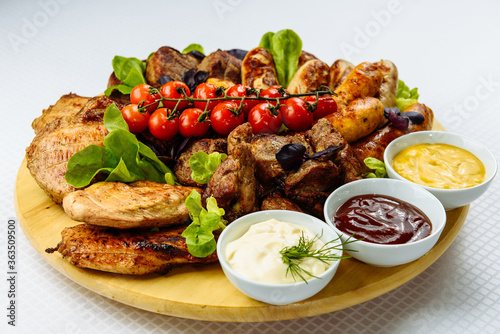 plate with fried meat, a wooden plate on a white tablecloth with fried meat, steak, barbecue, tomatoes and sauce
