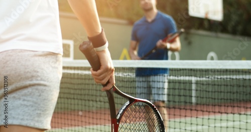 Happy young couple playing tennis on tennis court, close up view of hands with racket.