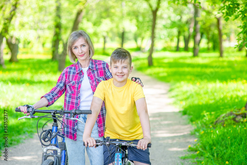 Portrait of a happy sporty family holding bikes in a summer park. Smiling woman hugs her young son. Empty space for text