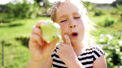 People and food: Beautiful caucasian girl eat a green cucumber. On the background a field with cucumbers. She smiles and laughs and grimaces. The sun is shining in the back