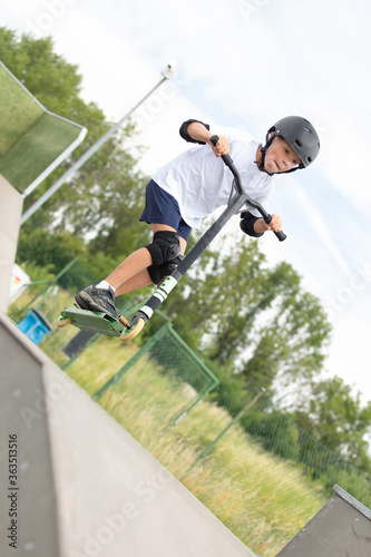 The boy jumps on a scooter.