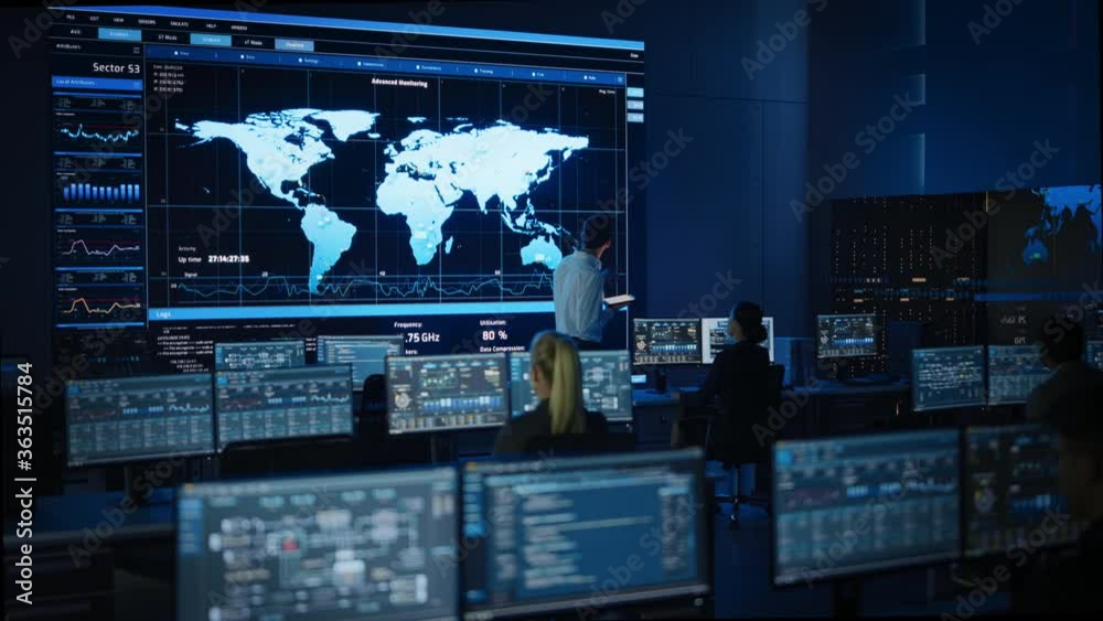 Project Manager Uses Digital Tablet Talks with Computer Scientist Looks at Big Screen Display Showing Infographics Global World Map Data.Telecommunications Control Monitoring Room with People Working