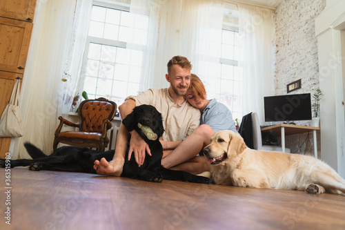 young couple with dogs sitting on the floor of their flat and having fun. dogs playing with their toys. man and woman hug each other and spend leisure time with their dogs