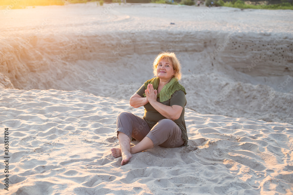 happy older woman meditate on a sand outside in summer