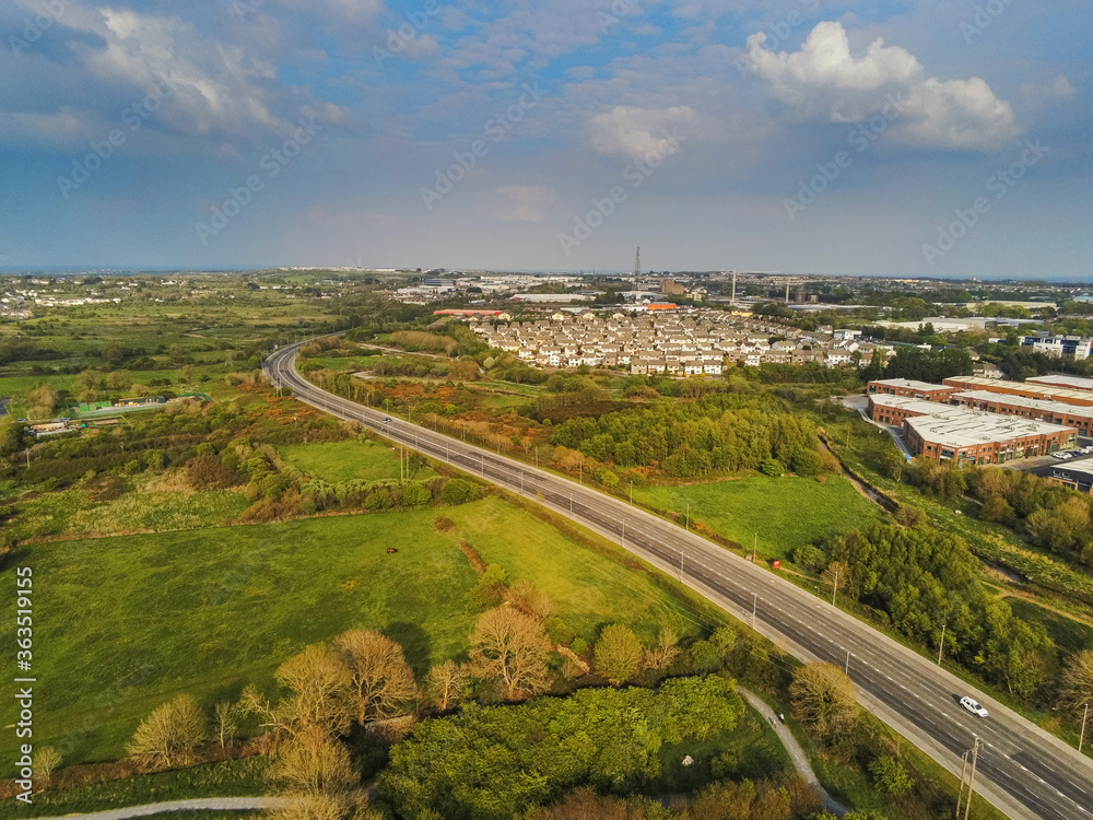 Empty highway near Galway city, Blue cloudy sky, Houses and commercial property on the right. Warm sunny day, Aerial view.