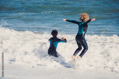 Two friends kids enjoying a funny surf day in the shore of a sunny beach in their coastal holidays 